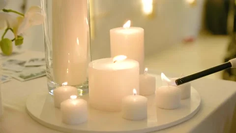 Close-up of lighting white candles of different sizes standing on a round stand. Stock Footage 288106313