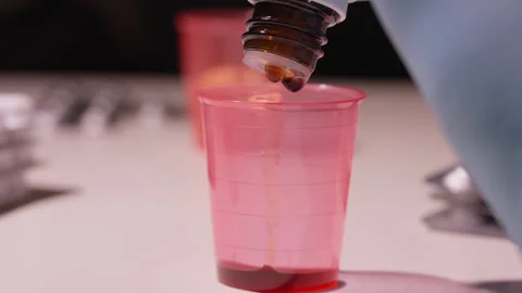 Close-Up of Liquid Drops Falling from Bottle into Medicine Cup Stock Footage 338364901