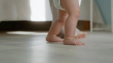 Close-up, little baby taking first steps, walking with mom next to him Stock Footage 303040439