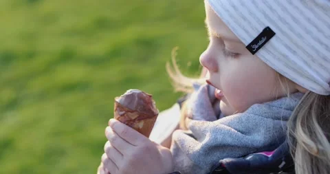 Close-up little blonde eats ice cream in a waffle cup outside Stock Footage 130433538