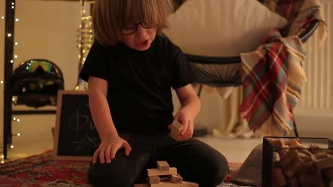 Close Up of Little Boy Plays Jenga Tower On Carpet in moody room Stock Footage 145335885