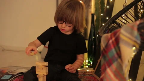 Close Up of Little Boy Plays Jenga Tower On Carpet in moody room Stock Footage 145336087