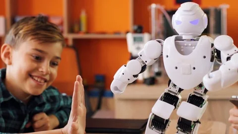 Close up of little white robot doing kicks to the kids hands on the table in the Stock Footage 82481177