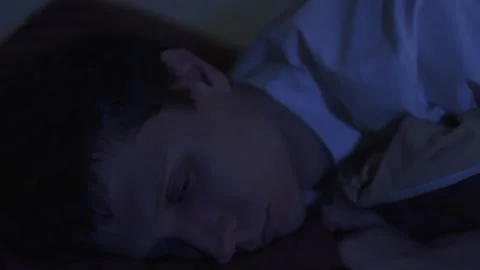 Close-up of a lonely man lying awake at night, staring into the dark with tired Video stock 321730811