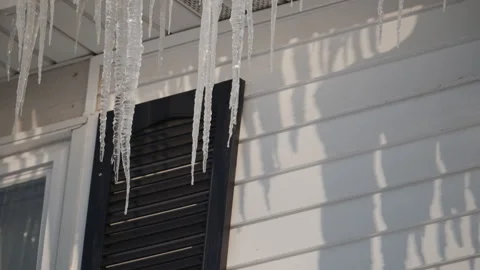 Close up of long, sharp icicles hanging from the edge of a snow-covered roof on Stock Footage 324249395