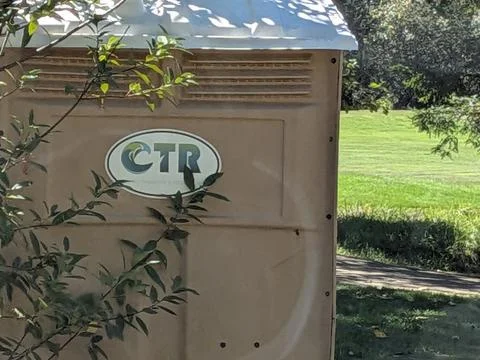 An up-close look at a light brown CTR portable restroom on green grass Photos
