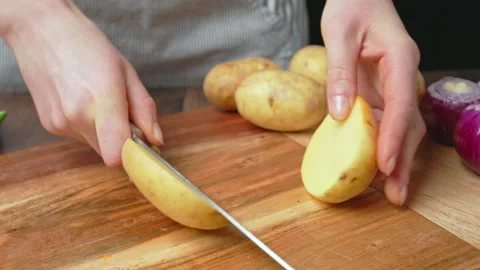 A close-up look of slicing fresh potatoes on a wooden cutting board in 4k. Stock Footage 145114154