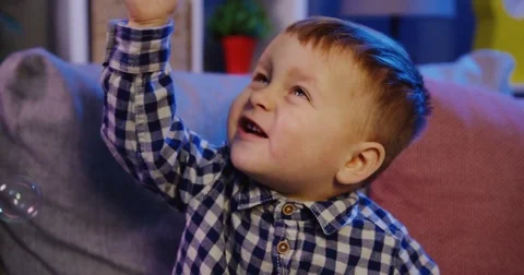 Close up of the lovely small boy sitting on the couch and having fun with soap Stock Footage 82920836