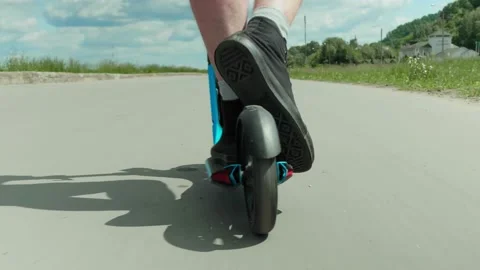 CLOSE UP, LOW ANGLE: Man rolling on a scooter on empty road and pushing off Video stock 133060245