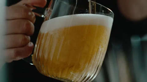 A close-up, low-angle shot of light golden beer being poured into a glass mug. Stock Footage 301279603