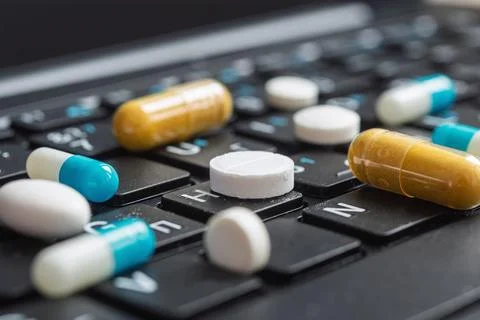 Close low angle view of pills on computer keys shows modern dependence on Фото