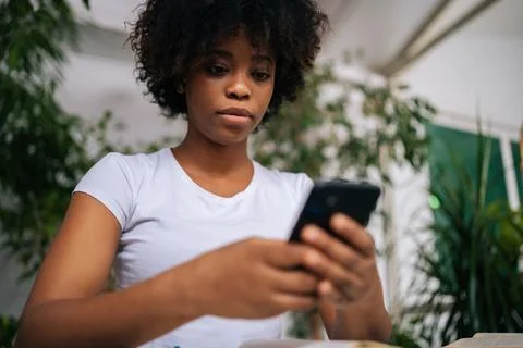 Close-up low-angle view of serious African young woman holding mobile phone in Stock Photos