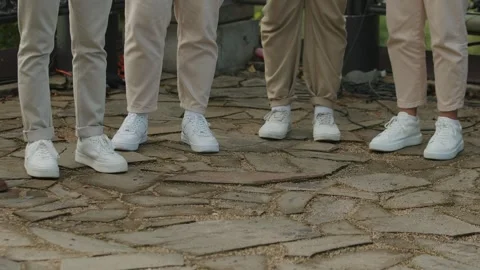 Close-up of lower legs of group of men in white sneakers and beige trousers Vidéo 317226482