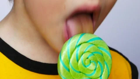 Close-up of a lower part of a face of a little boy licking big twisted lollipop Stock Footage 147432512