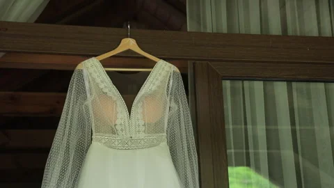 A close-up of a luxurious boho-style wedding dress hanging on the door of a Stock Footage 322558605