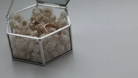 A close-up of a luxurious glass wedding ring box filled with flowers, with gold Stock Footage 321897094