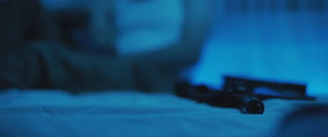 Close up of M16 rifle lying on a bed, with PTSD soldier siiting on bed in the Stock Footage 147537584