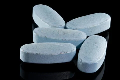 Close-up macro shot of five blue oval pills scattered on a reflective black.. Stock Photos