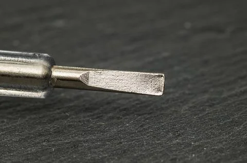 Close-up macro shot of a flathead screwdriver tip on a dark textured surface Stockfoto's