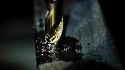 Close-up macro shot of a metallic twisting drill bit drilling a dark metallic Stock Footage 338402312