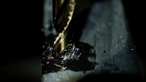 Close-up macro shot of a metallic twisting drill bit drilling a dark metallic Stock Footage 338402324