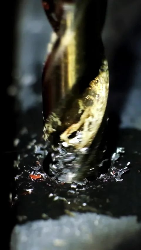 Close-up macro shot of a metallic twisting drill bit drilling a dark metallic Stock Footage 338402345