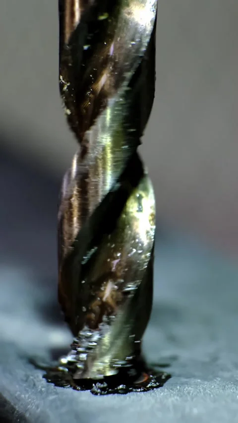 Close-up macro shot of a metallic twisting drill bit drilling a dark metallic Stock Footage 338402359