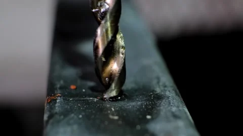 Close-up macro shot of a metallic twisting drill bit drilling a dark metallic Stock Footage 338402392