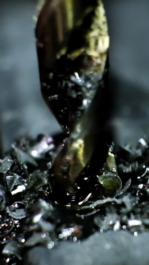 Close-up macro shot of a metallic twisting drill bit drilling a dark metallic Stock Footage 338402401