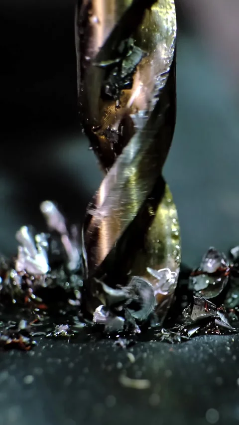 Close-up macro shot of a metallic twisting drill bit drilling a dark metallic Stock Footage 338402409
