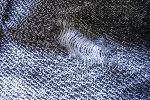 A close-up macro shot shows a rip in a dark woven fabric. Stock Photos