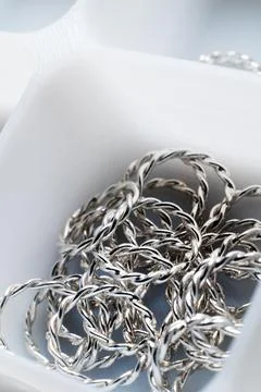 Close-up macro shot of small silver jewelry pieces lying in a white mesh box Stock Photos