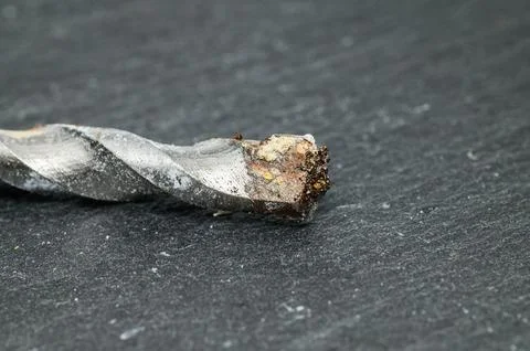 Close-up macro shot of a worn and dirty drill bit tip on a dark textured su.. Stockfoto's