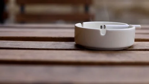 Close up macro view of cigarette in white ashtray on wooden table on blur backgr 스톡 동영상 118506454