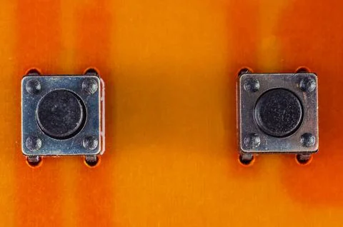 Close-up macro view of two small tactile push buttons on an orange circuit .. Stock Photos