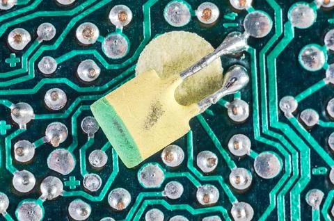 Close-up macro view of a yellow capacitor soldered onto a green circuit boa.. Stock Photos