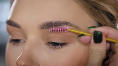 Close-up. Make-up artist combs and styles the eyebrows of a young blonde woman Stock Footage 235659602