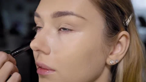Close-up of a makeup artist applying concealer under the eyes of a young blonde Stock Footage 235618447