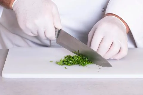 Close up of a male chef with gloves using a kitchen knife to chop some parsle Stock Photos
