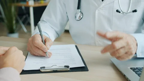 Close-up of male doctor filling in medical chart talking to female patient in Stock Footage