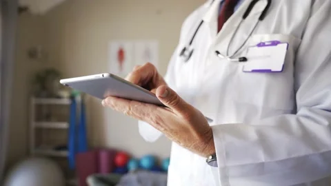 Close up of male doctors hands browsing on digital tablet in consultation room Stock Footage 135720646
