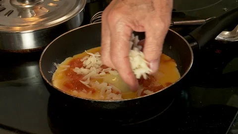 Close up of male hand adding cheese to an omelette cooking on stove top Stock Footage 128451415