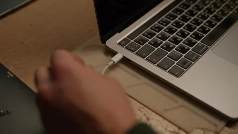 Close-up of male hand plugging usb-c cable into modern silver laptop on table Stock Footage 301400464