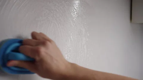 Close-up of male hand using blue sponge with detergent to clean white wall in Stock Footage 305997610