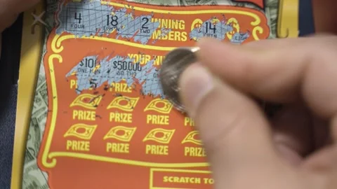 Close up of a male hand using a coin to scratch numbers on a lottery card. Vidéo 257029251
