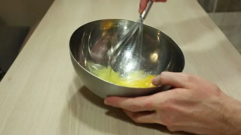 Close-up male hands beating eggs with a whisk in a metal bowl. Stir eggs cooking Stock Footage 152902198