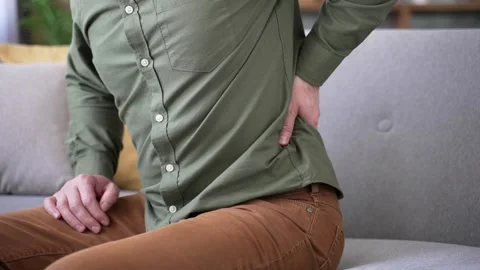 Close-up of male hands holding and massaging lower back while sitting on sofa  Stock Footage 328706249