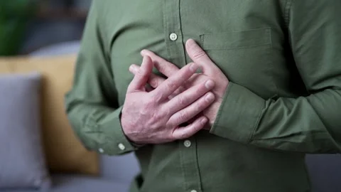 Close-up of male hands holding chest while suffering from heart attack at home.  Video stock 328706207