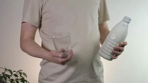 Close-up of male hands holding an empty glass and an open milk bottle ideal for Stock Footage 314424507