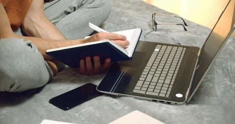 Close-up of male hands making notes in a notebook studying with a laptop at home Stock Footage 129092689